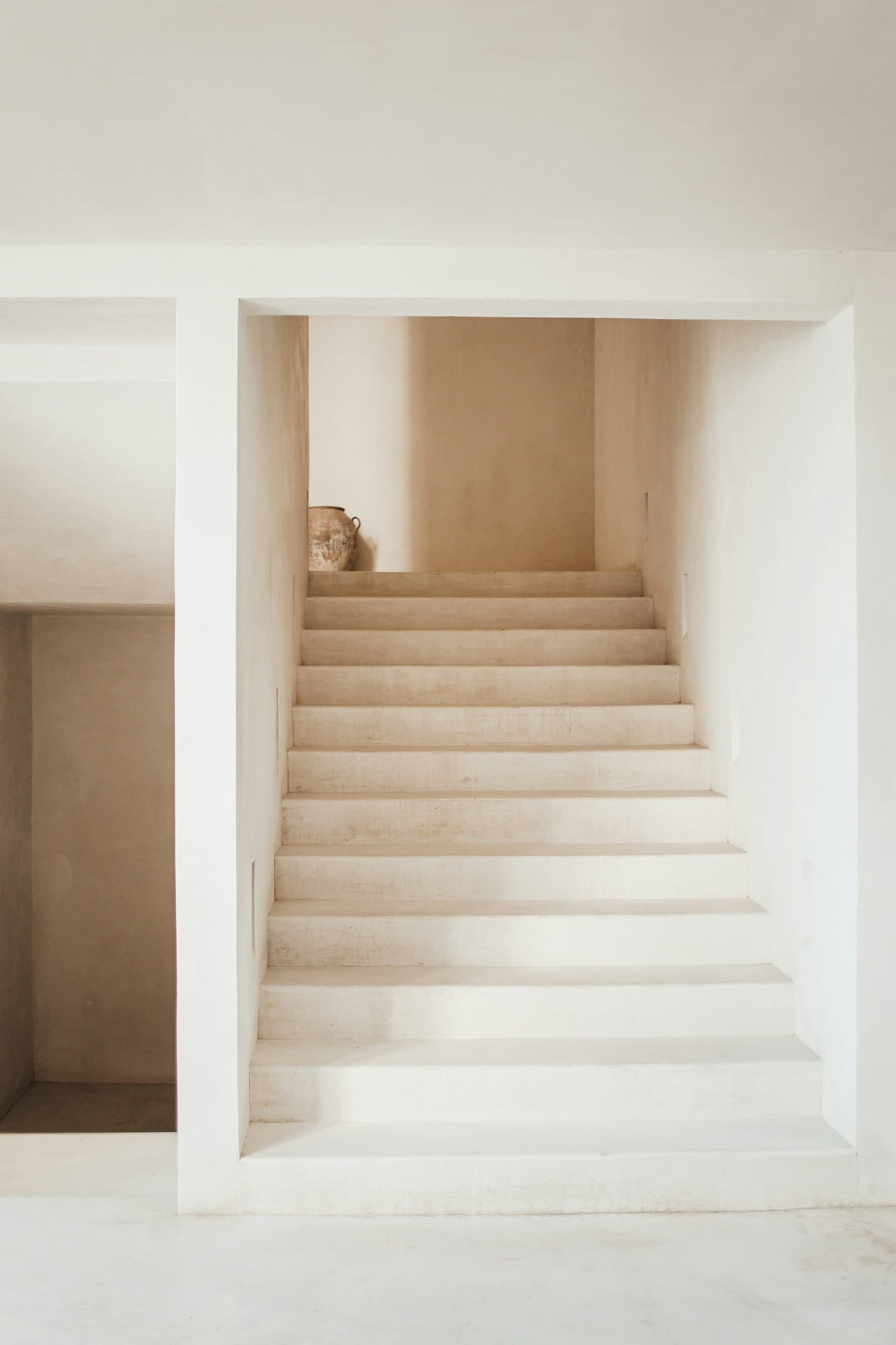 A minimalist staircase with white concrete steps leading to a landing with a vase
